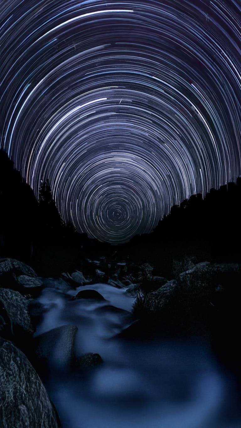 Long exposure captures stunning star trails above a tranquil river in the forest. Perfect for astronomy and nature enthusiasts.